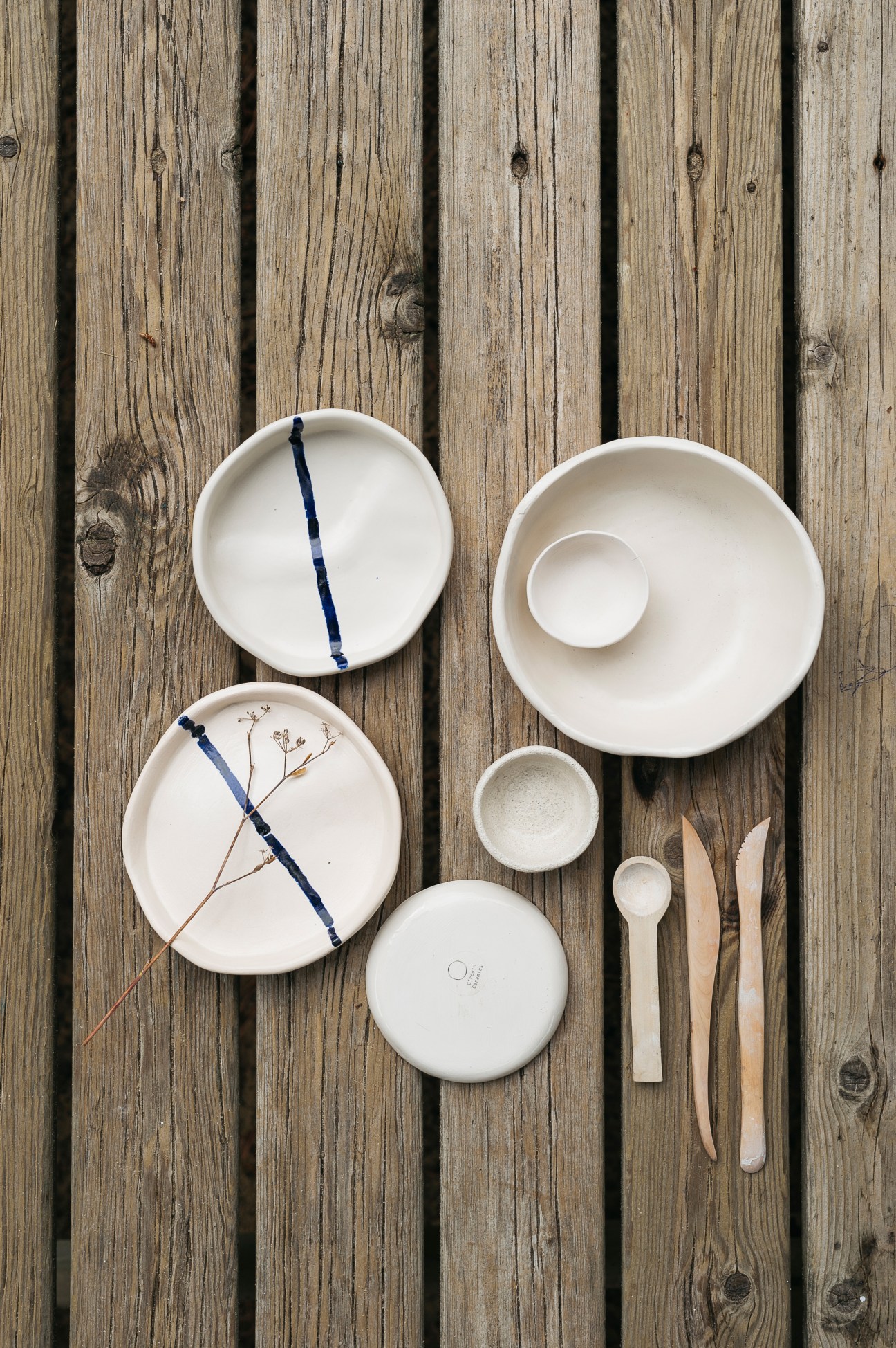White ceramic dishes and bowls by Margarida Almeida of Circulo Ceramics arranged on weathered wood, including vide poche pieces with blue accents and wooden utensils.