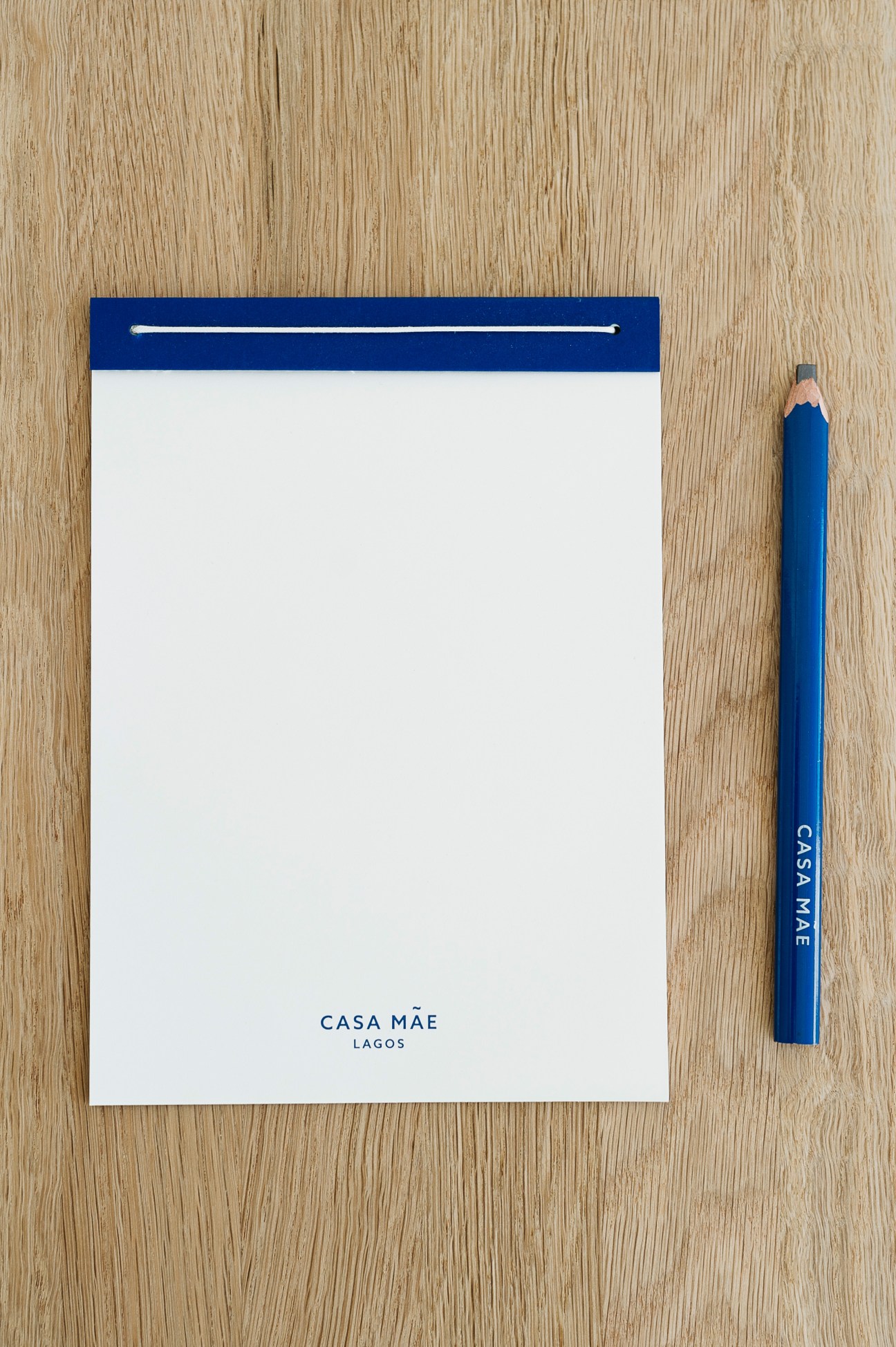 Casa Mãe notebook with blue header and matching pencil on wooden surface.