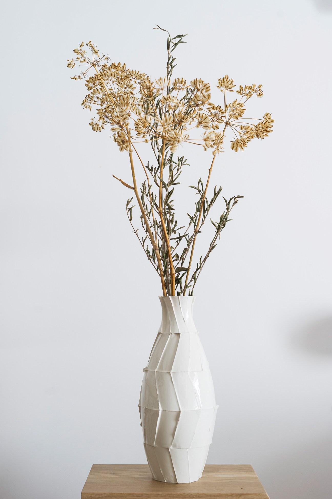 White ceramic vase with geometric wave pattern holding dried golden flowers and green stems.