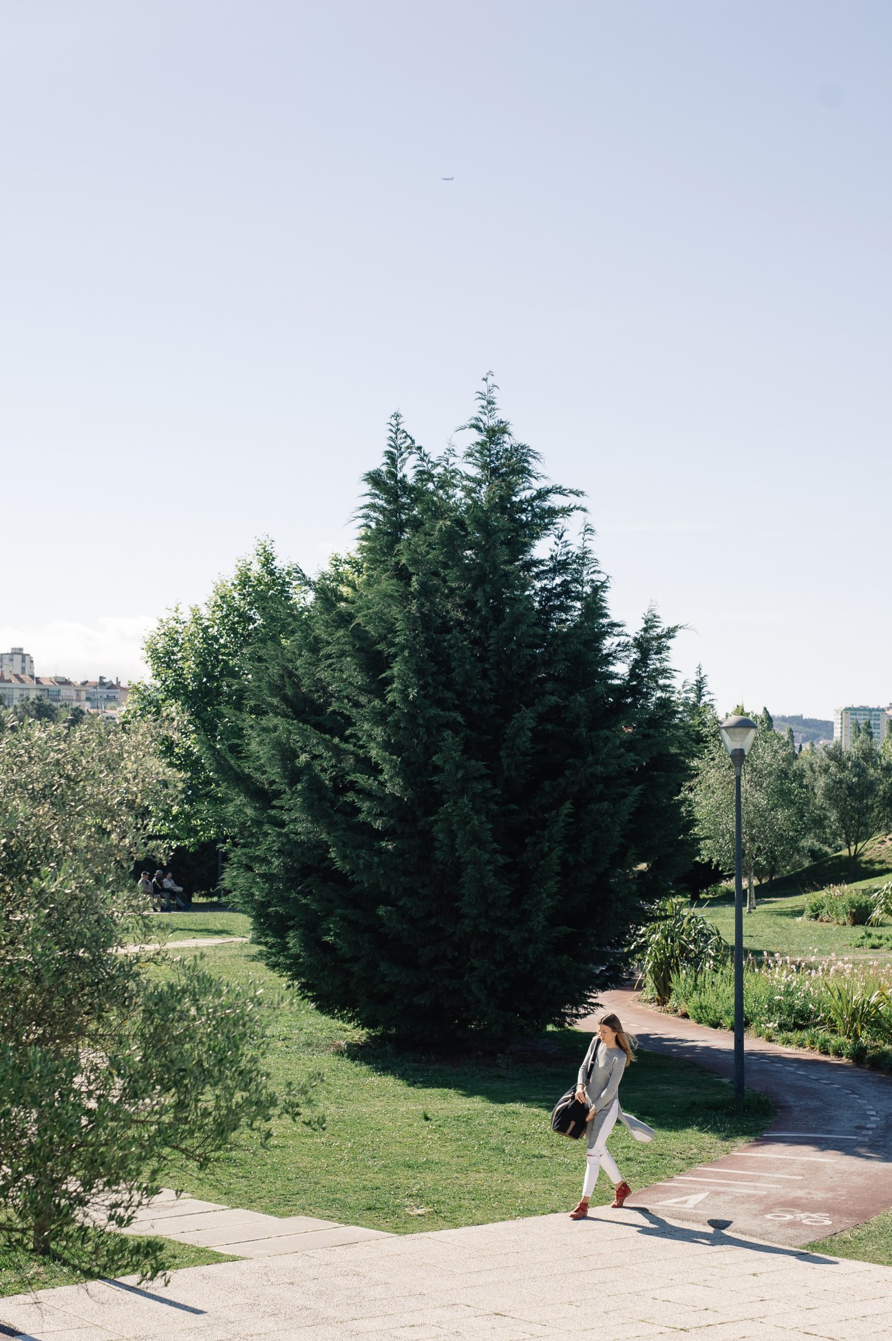 A woman jogging through a green park with mature trees and landscaped pathways in Lisbon.