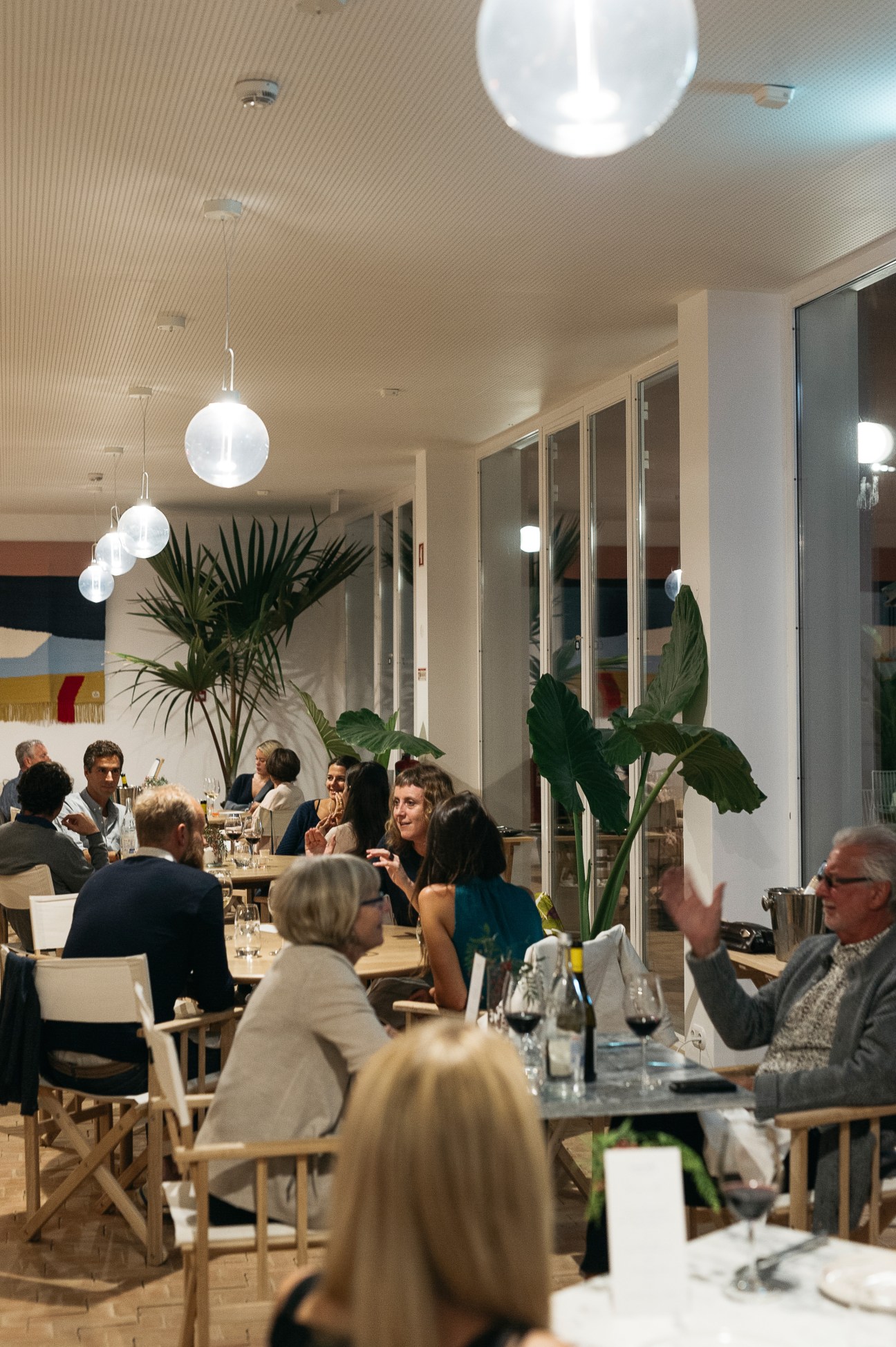 Guests dining in Casa Mãe restaurant with pendant lights and potted plants.