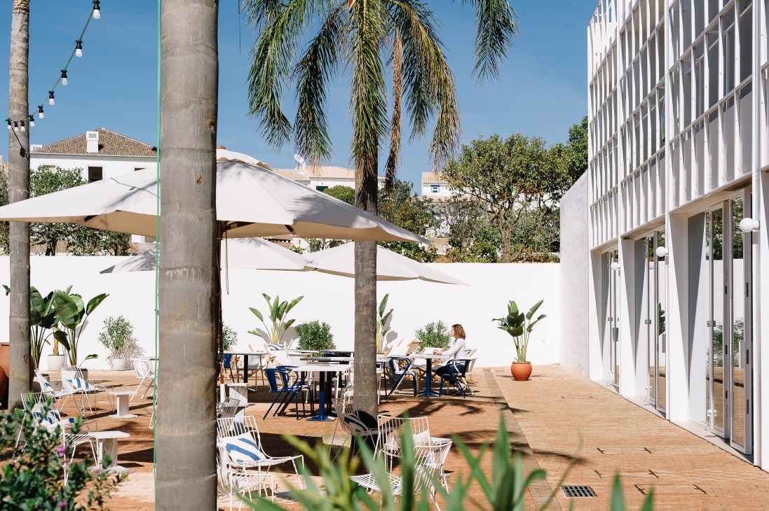 Casa Mãe hotel restaurant terrace with white umbrellas, wooden deck, and modern white building in Lagos, Portugal.