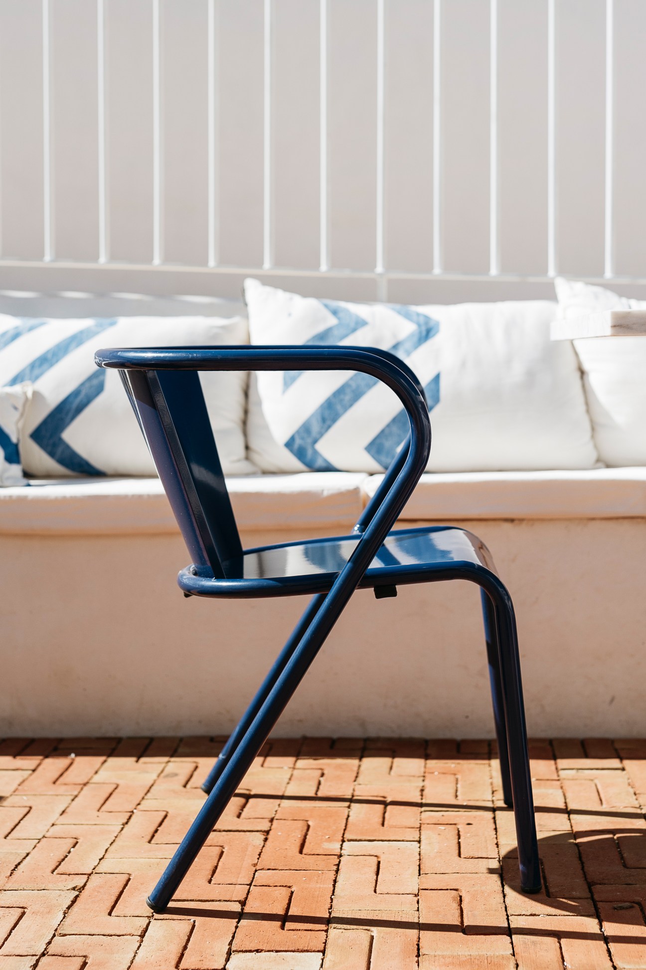 Blue metal café chair by Portuguese brand Adico on terracotta tiles with cushioned seating behind.