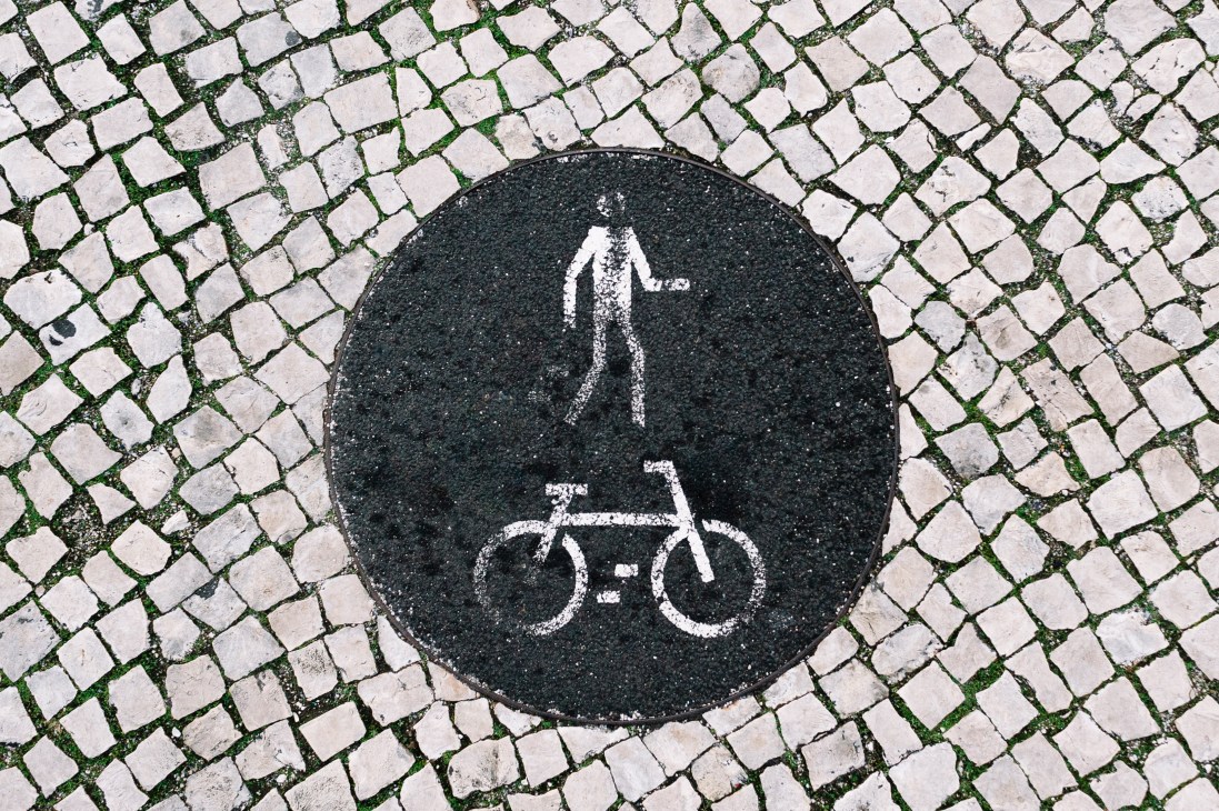 Black circular street marking with white stencilled bicycle and pedestrian symbols on cobblestone pavement.