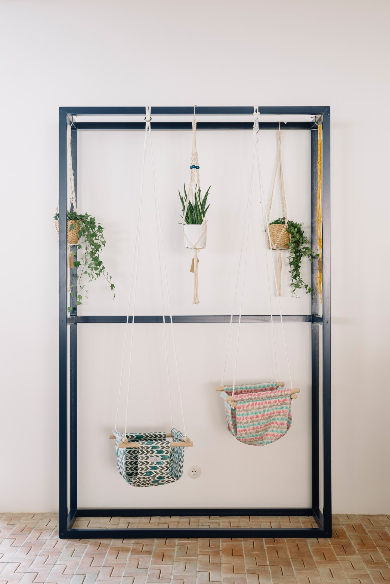 Metal frame clothes hanger repurposed as a plant display with hanging potted plants and woven baskets.