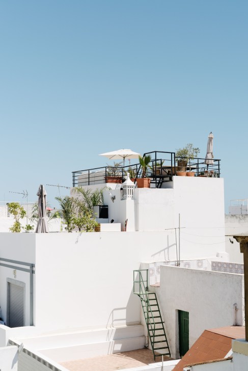 White-walled cubist building with terracotta pots and vegetation on rooftop terraces under clear blue sky in Olhão's old town.