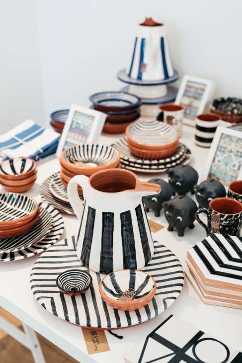 Casa Cubista ceramic tableware collection displayed on a white surface, featuring striped plates and bowls in terracotta, black, and white.