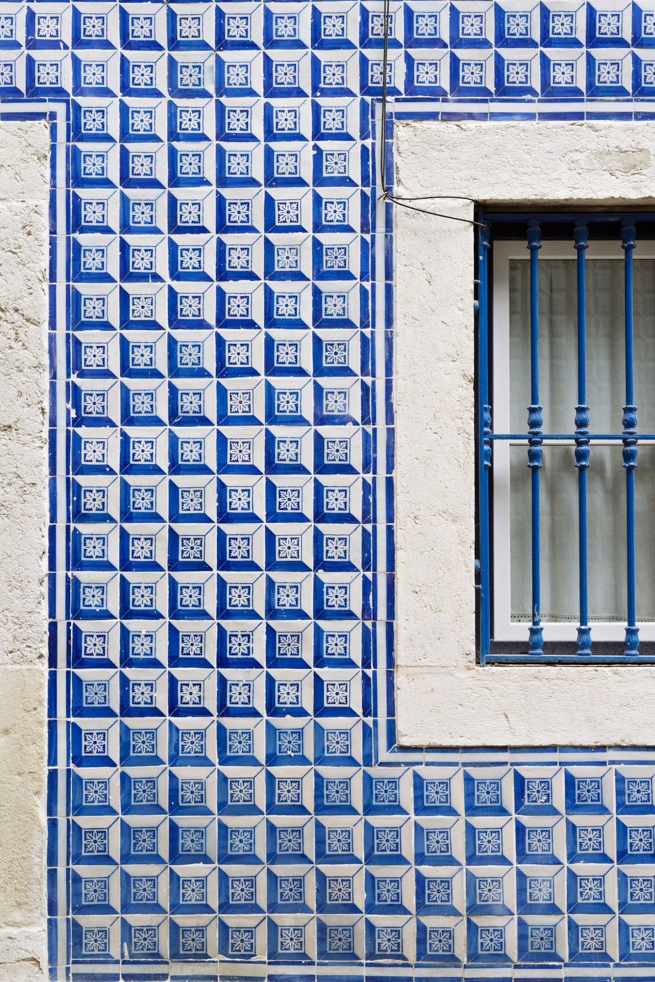 Blue and white geometric tile pattern on building facade with window in Lisbon.