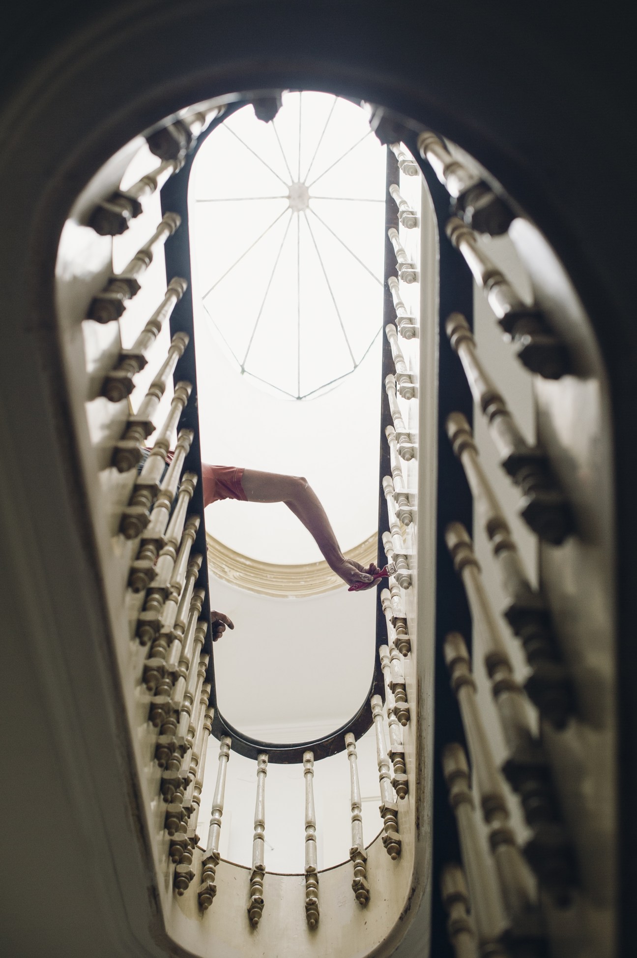 Upward view through a spiral stairwell with ornate wooden balustrades and natural skylight, Porto renovation project.