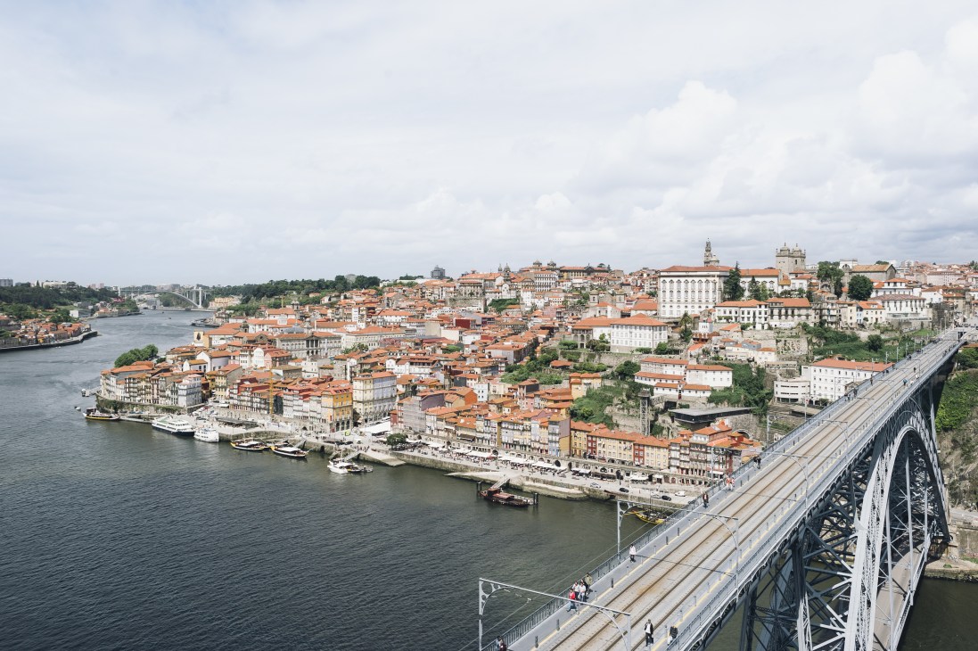 Panoramic view of Porto's historic centre with terracotta-roofed buildings along the River Douro and an iron bridge spanning the water.