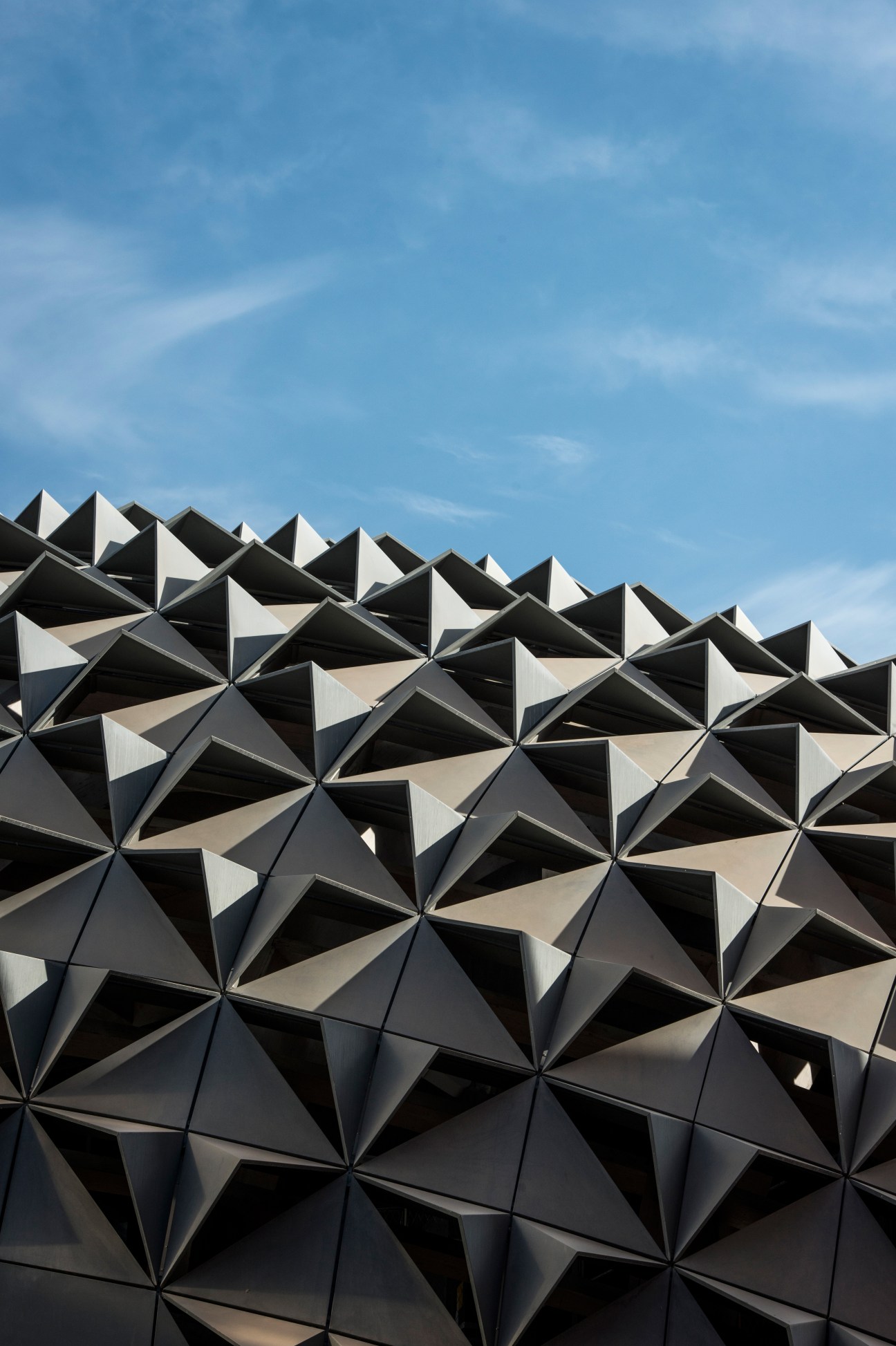 Geometric zinc-clad roof of the Knowledge Center with pyramidal forms against blue sky.