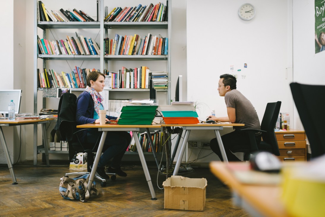 Two editors work at a desk in the Falter offices, with shelves of books behind them.