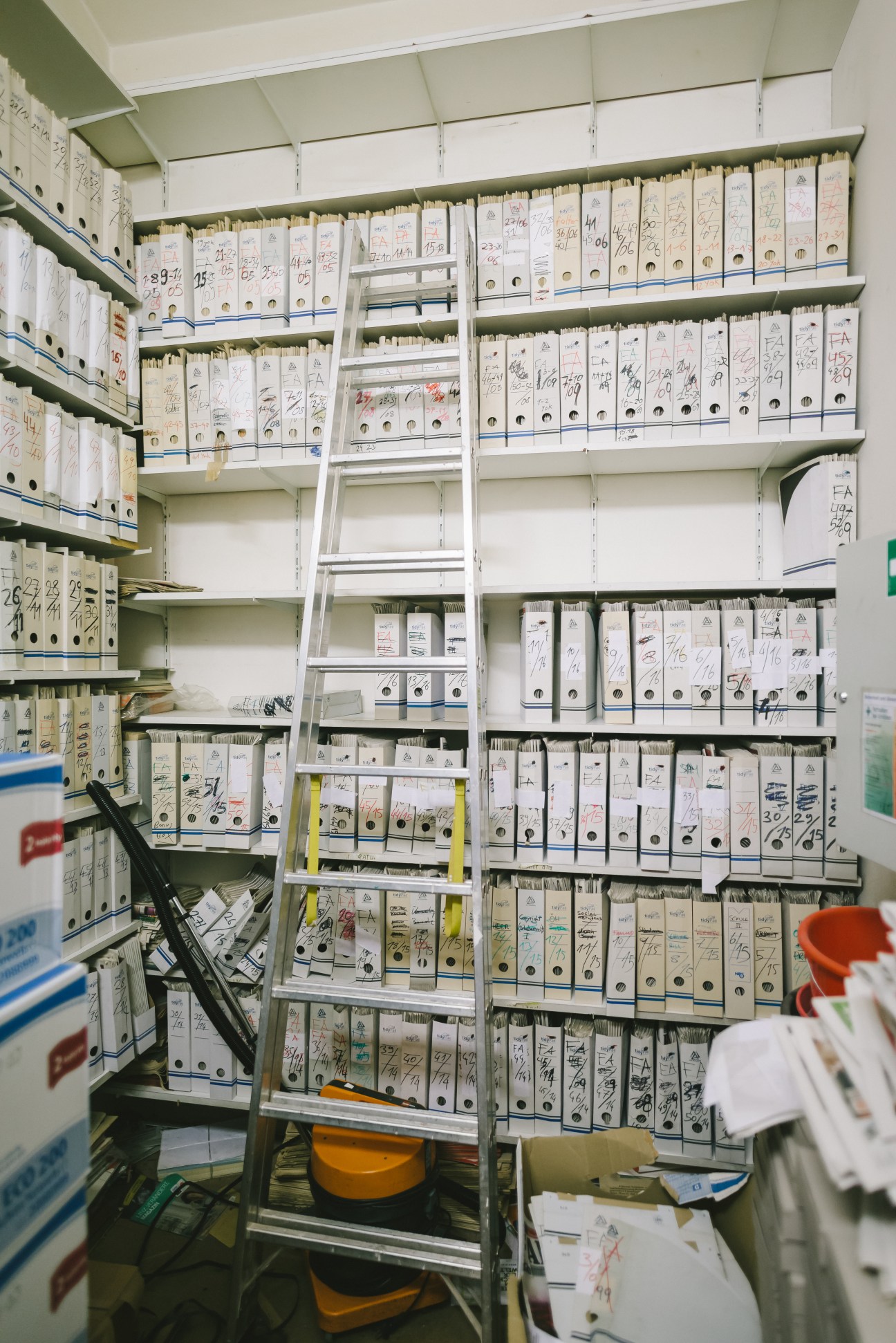 Shelves of archived Falter magazine issues organized in white boxes with handwritten labels and a ladder.