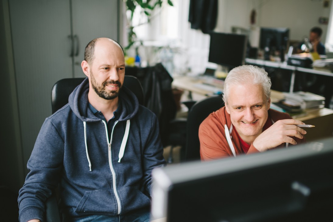 Two designers review layouts at a computer workstation in the Falter office.