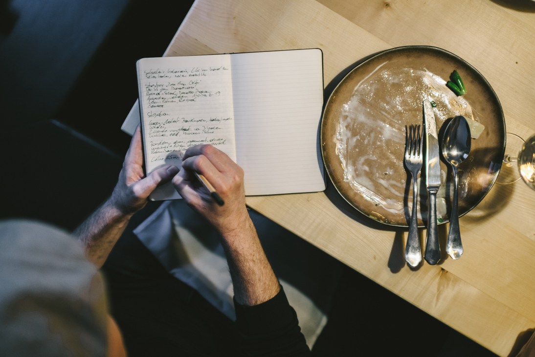 Food critic Florian Holzer taking notes in a notebook at a restaurant table with a plate of food.