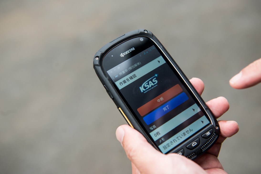 A Kyocera handheld device displaying the Kubota Smart Agri System interface with Japanese text and colored status indicators.