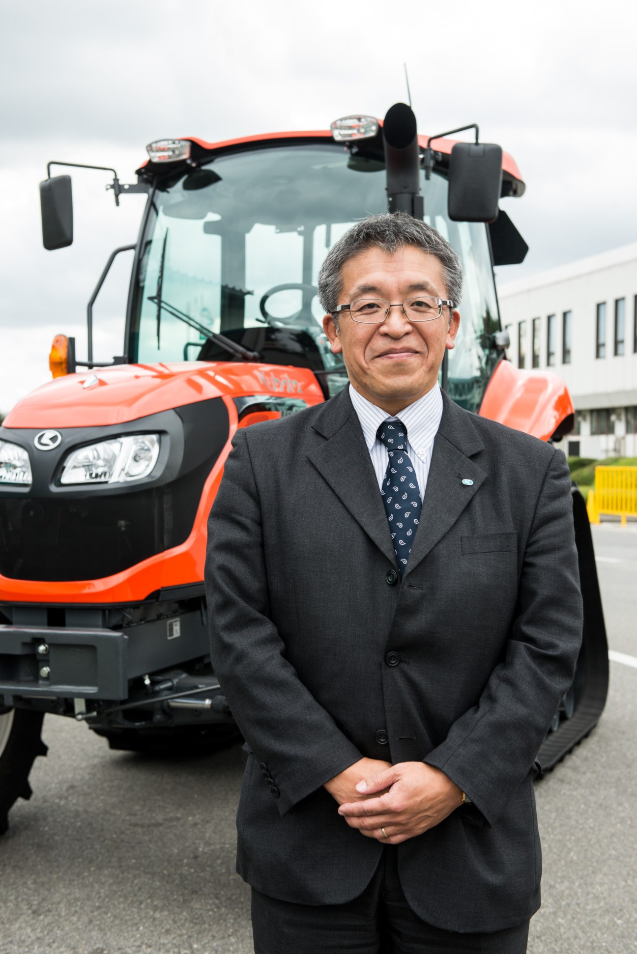 Yasuo Kammuri, Kubota's head of farm machinery for Japan, standing in front of an orange tractor.