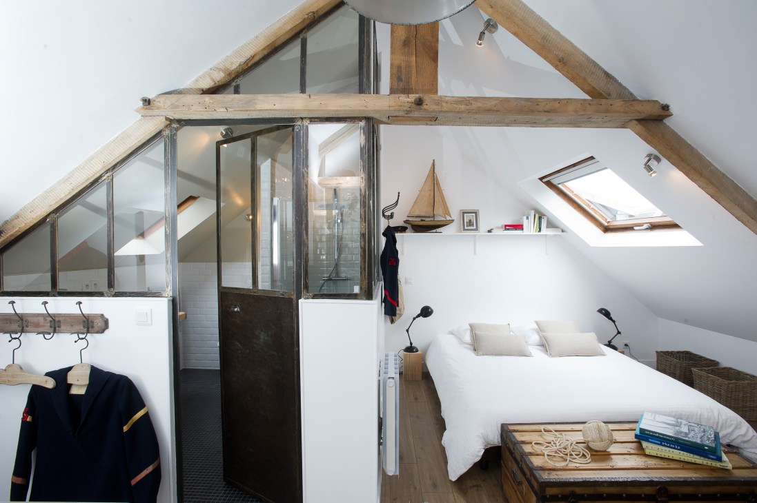 Attic bedroom with exposed wooden beams, white walls, and a bed with white linens beneath skylights.