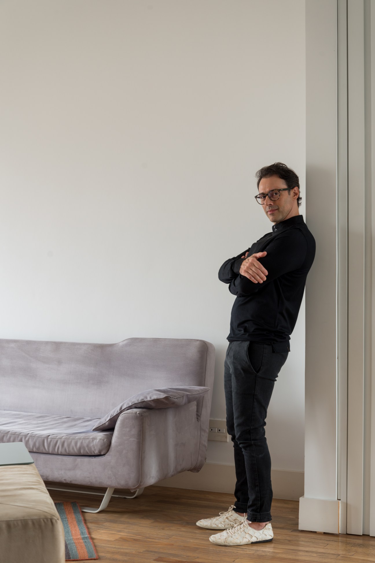Man in black shirt standing beside grey armchair in minimalist white interior