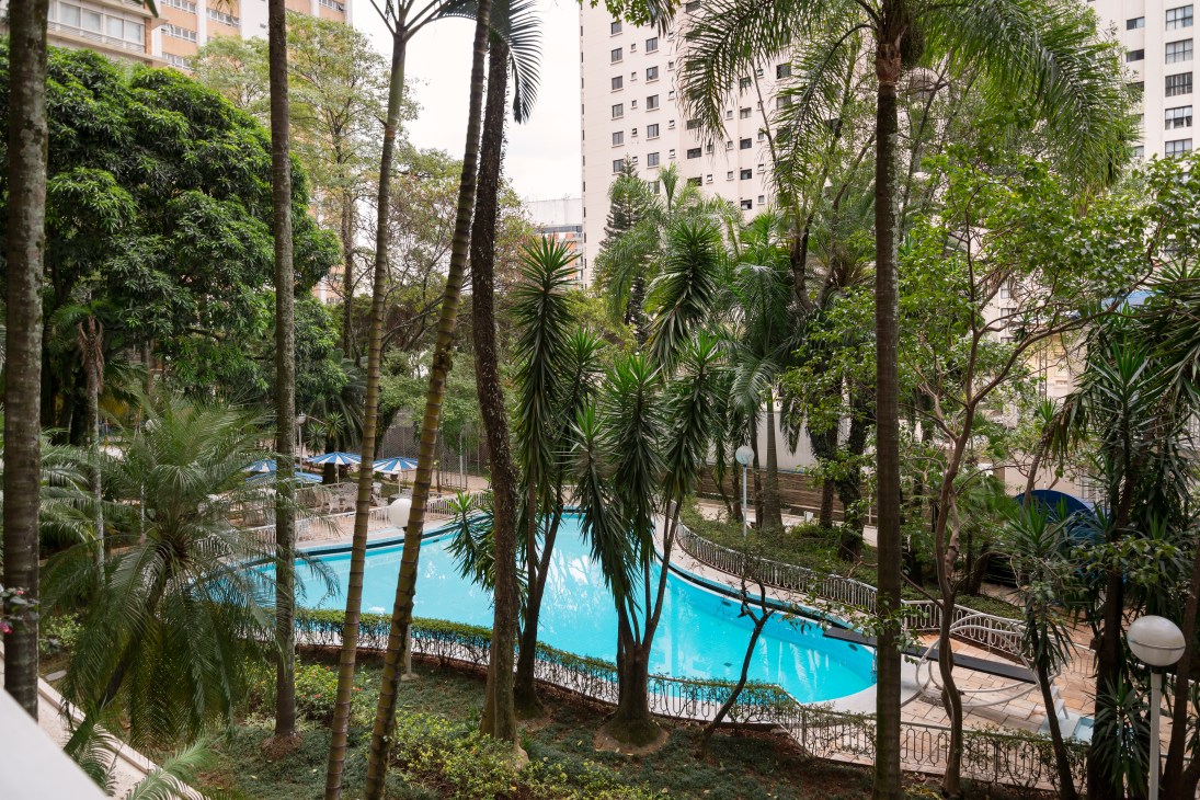 Splash-shaped pool surrounded by palm trees and tall buildings at the Bretagne Building in São Paulo.