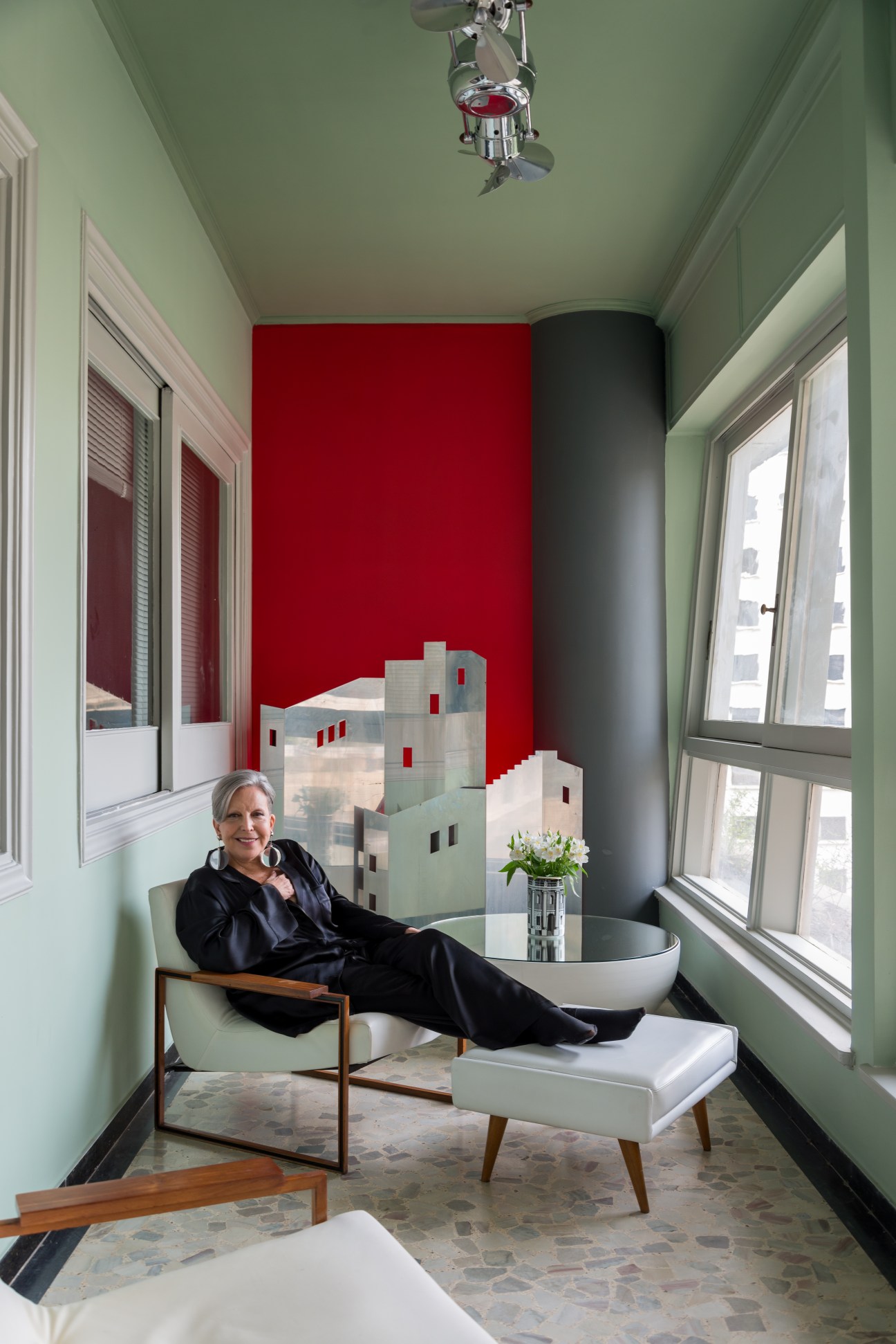 Fashion journalist Regina Guerreiro in her apartment with green walls, red accent wall, and architectural model.