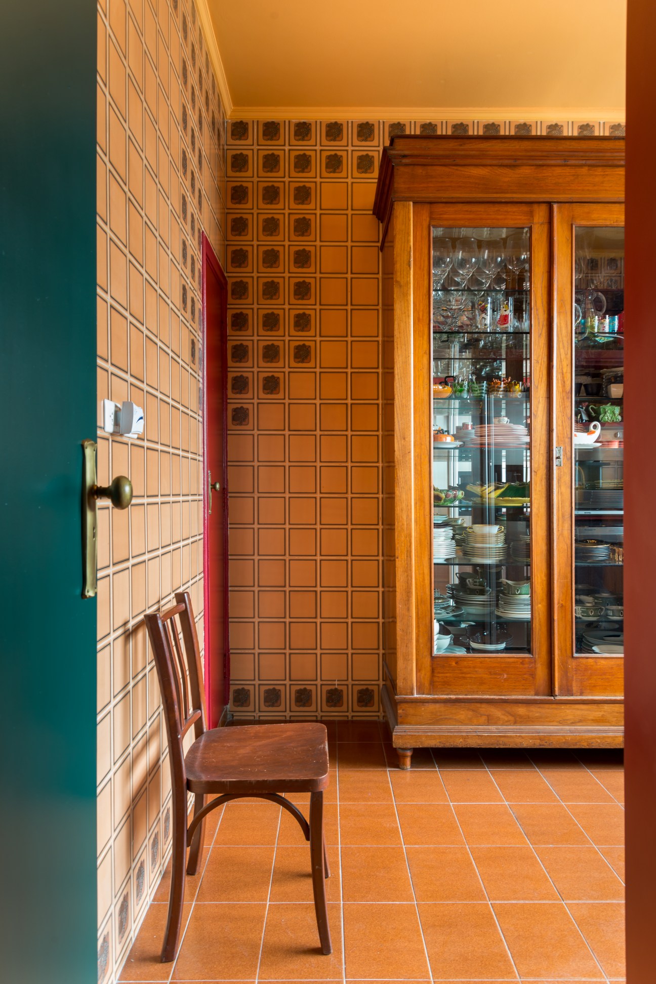 A 1958 kitchen with orange tiles, patterned walls, wooden cabinetry, and vintage furnishings in warm tones.