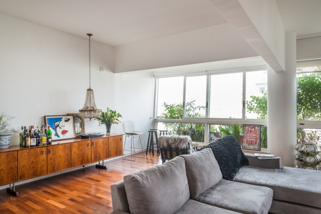 Modern living room with gray sofa, wooden sideboard, and large windows overlooking green terraces in the Bretagne Building.