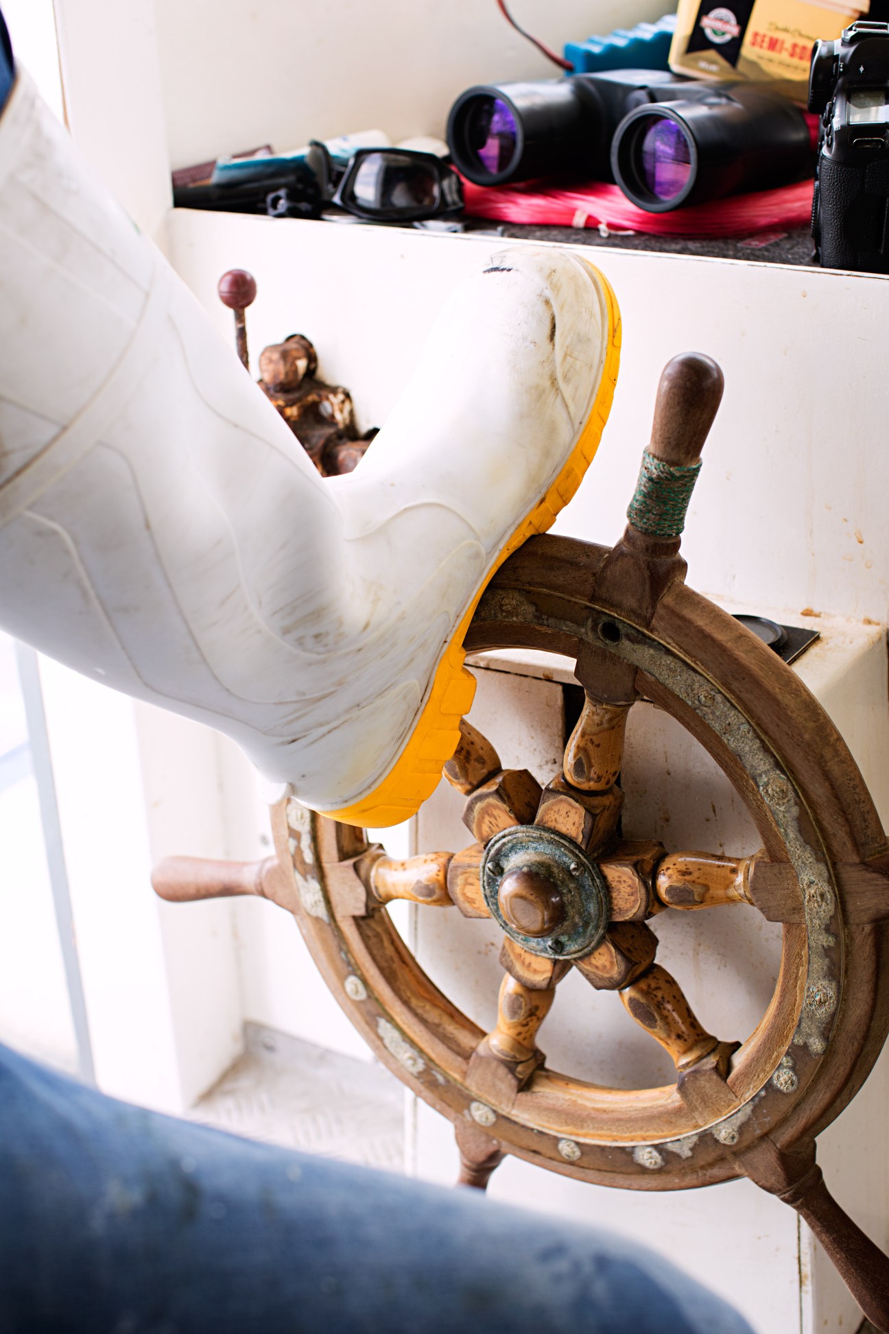 Ship's wheel and deck ornaments on a fishing boat with binoculars visible in background.