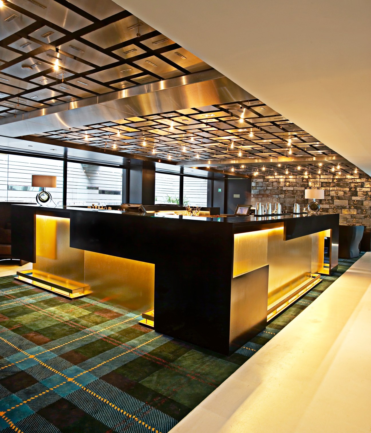 Modern hotel reception area with black and gold geometric design elements and grid ceiling lighting.