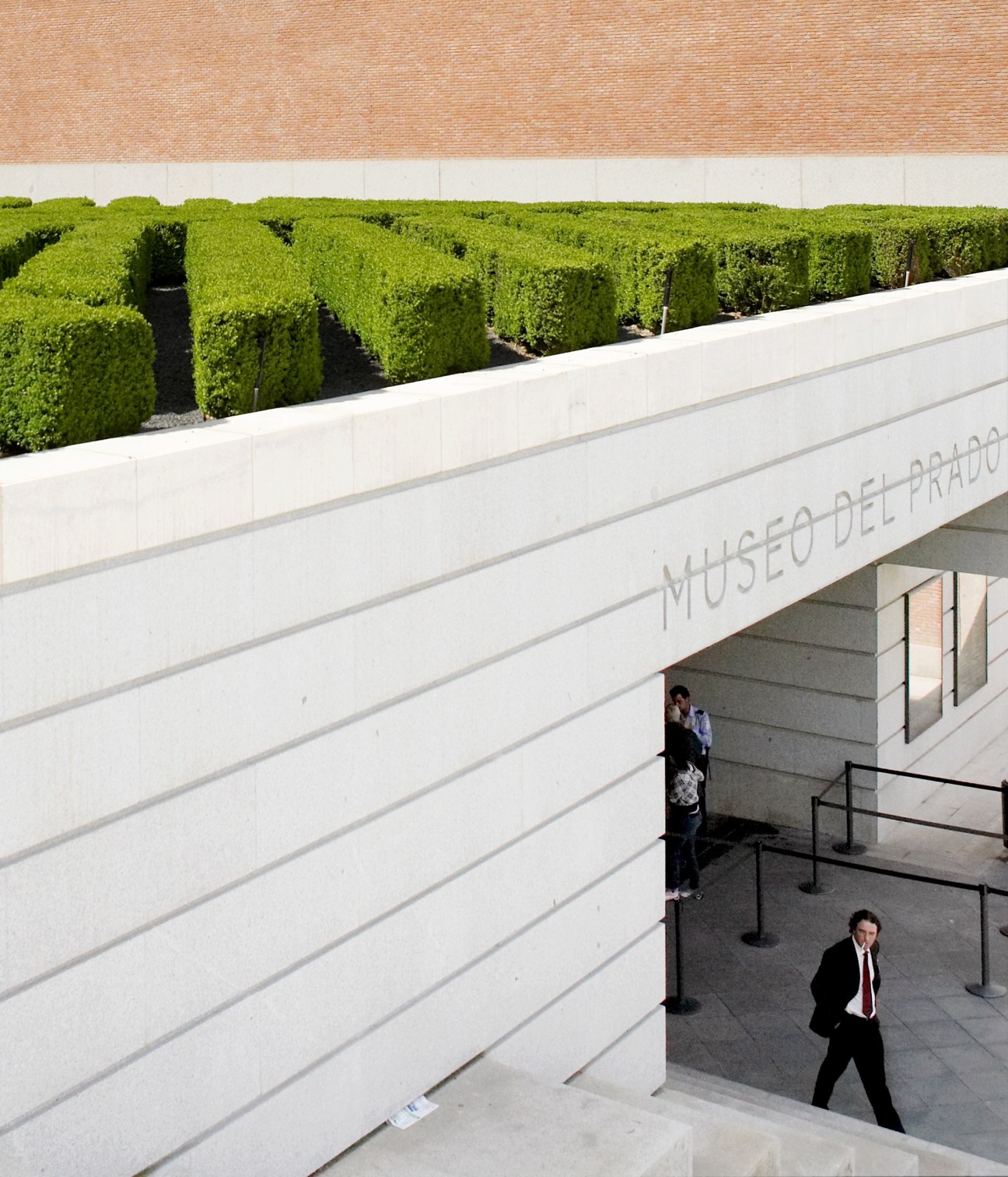 Exterior of Museo del Prado with white modern architecture, green hedges, and visitors on terrace.