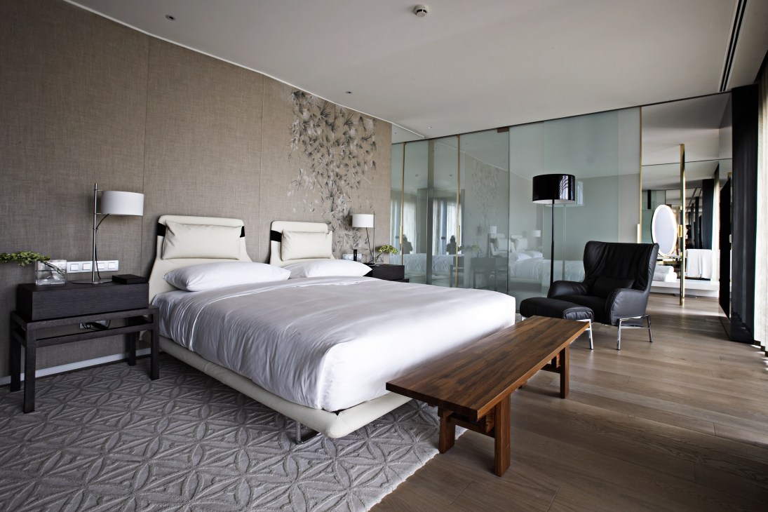 Modern hotel bedroom with minimalist design, white bedding, natural materials, and floor-to-ceiling mirror panels at Mandarin Oriental Barcelona.