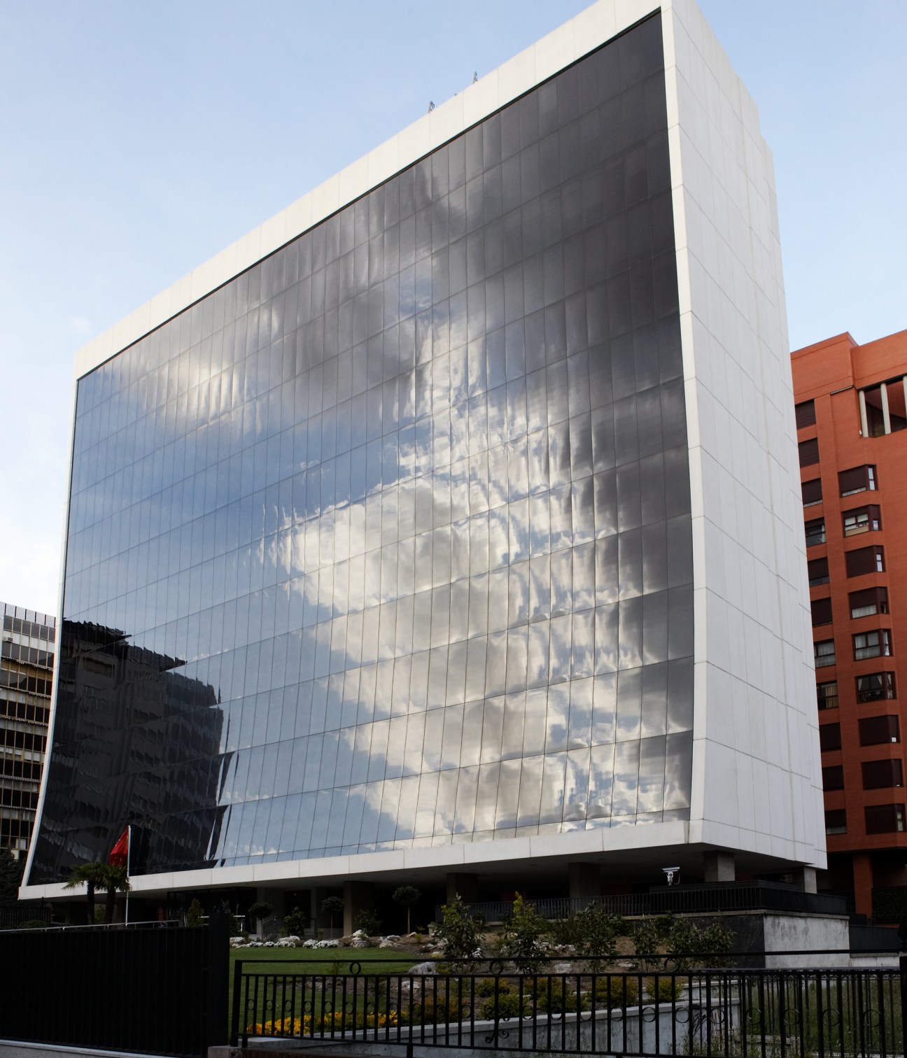 Modern glass and white facade building with cloud reflections, surrounded by older brick buildings.