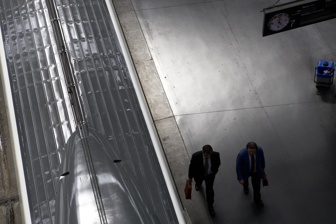 Two businessmen walk past the sleek silver exterior of a high-speed AVE train at a station platform.