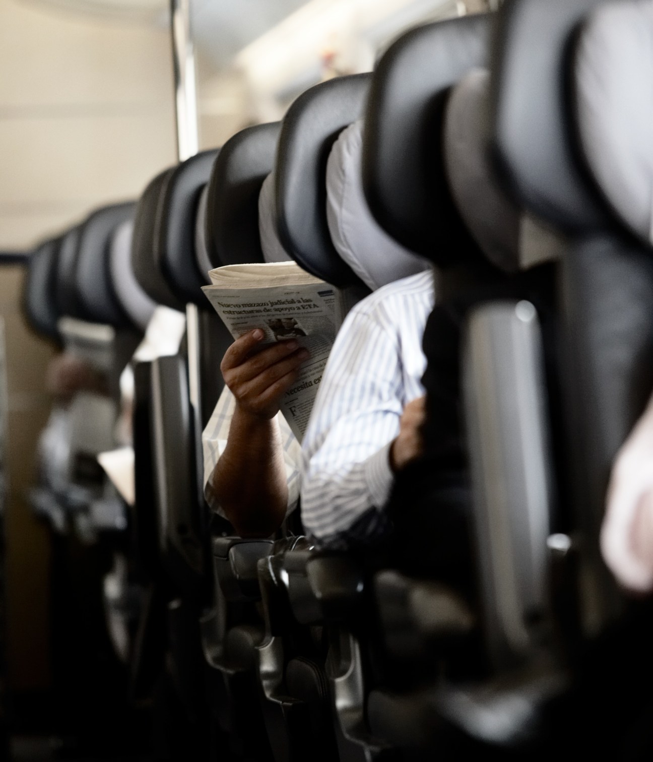 Passenger reading newspaper on Spanish AVE high-speed train surrounded by black and white seats.