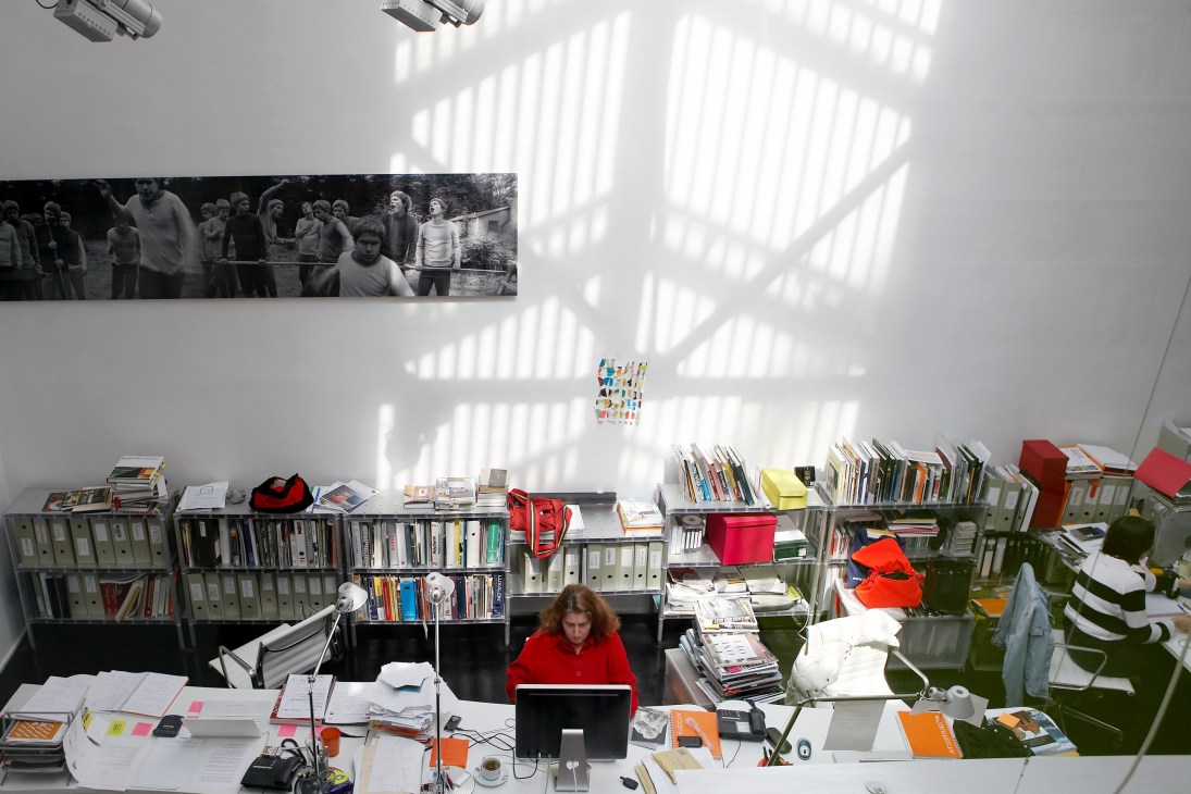 Architect Teresa Sapey works at her desk in a bright, minimalist office filled with books and colorful storage boxes.