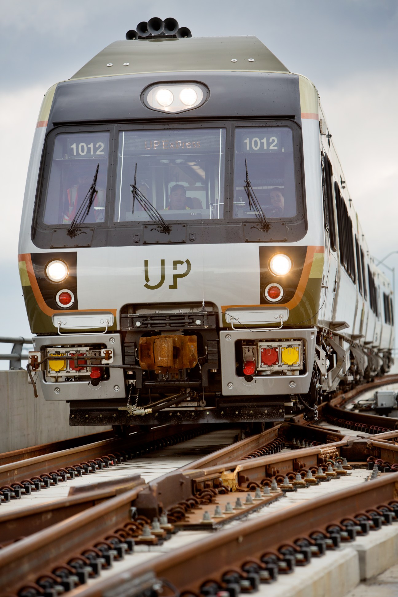 Front view of UP Express train with sage green, grey and orange livery on railroad tracks
