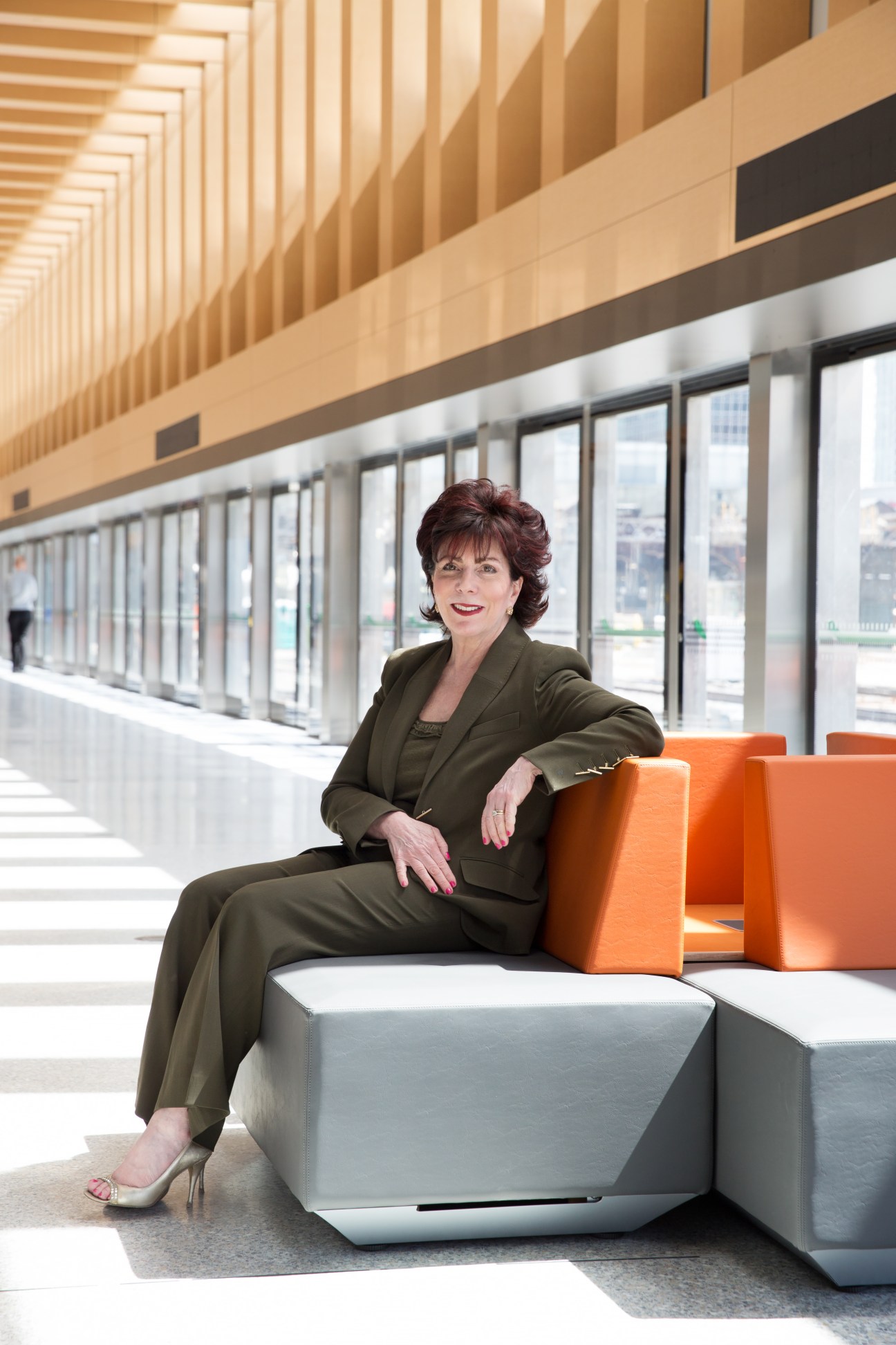 UP Express president Kathy Haley sits on orange and white modular seating in a modern station with wooden ceiling beams and large windows.
