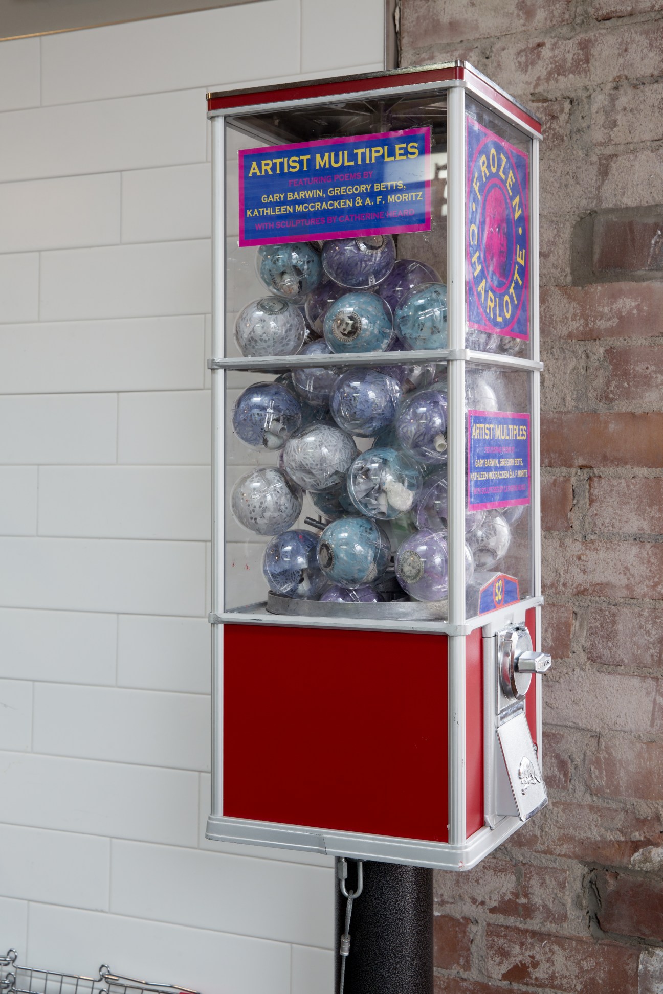 A red and white vending machine filled with blue and silver spherical art objects labeled 'Artist Multiples'.
