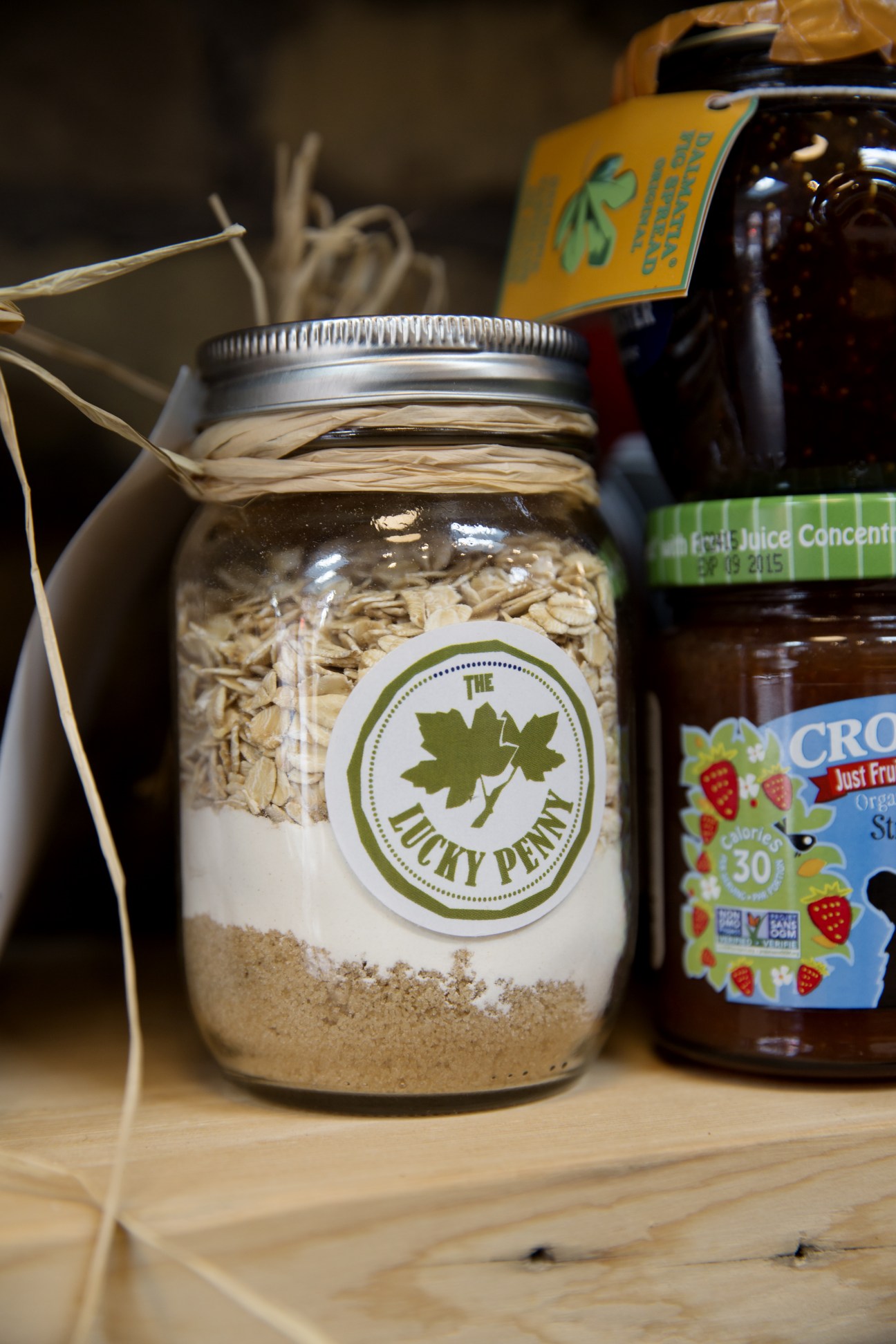 Pre-mixed oatmeal in a glass jar with The Lucky Penny label and leaf logo, surrounded by other pantry items.