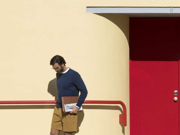 Man wearing Louis Vuitton jumper and Golden Goose shorts standing against yellow building with red door.