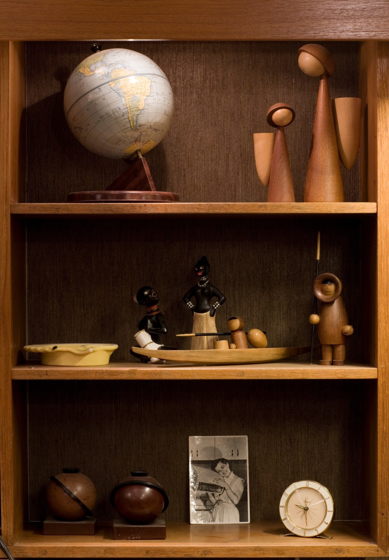 Wooden shelving unit displaying vintage Nordic design objects including a globe, teak figures, wooden vessels, and decorative items.