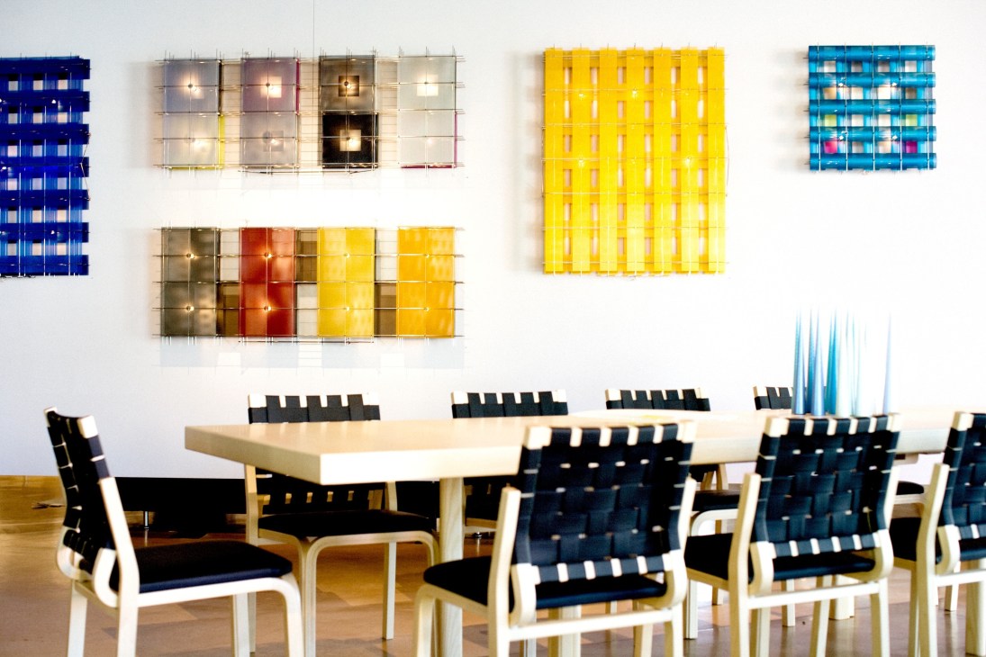 Modern gallery interior with colorful grid-pattern wall art installations above a light wood table and black chairs.