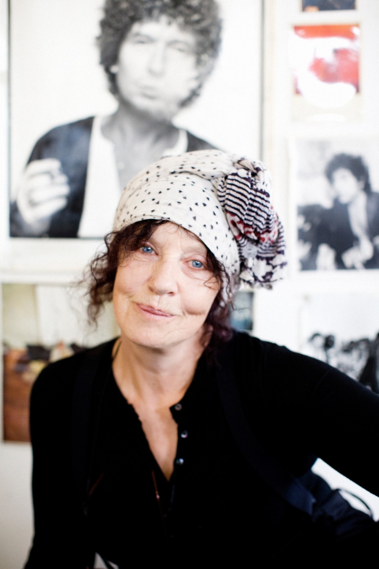 Woman wearing a polka dot and striped beanie standing in front of framed black and white photographs on a wall.