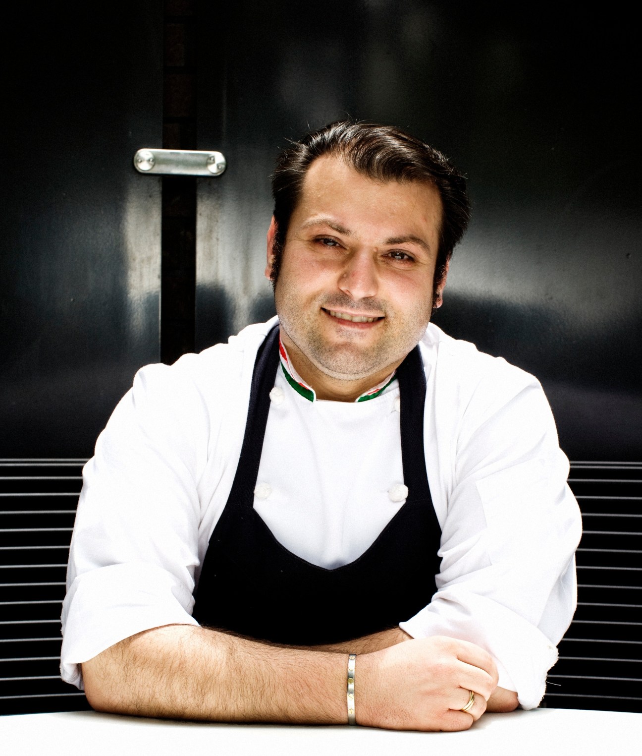 Portrait of Danny Russo, a chef wearing a white shirt and black apron, smiling at the camera.