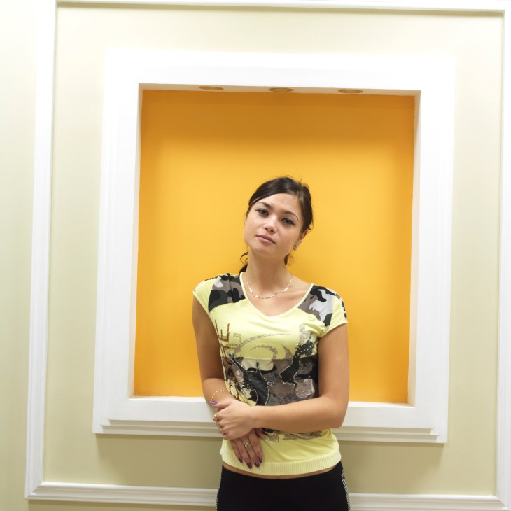 Young woman standing in front of a yellow-painted alcove wearing a graphic t-shirt.