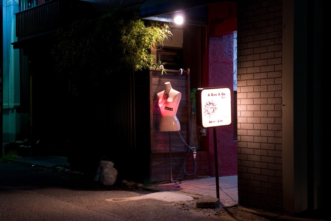 A Bao A Qu bar entrance at night with illuminated sign and mannequin in window display.