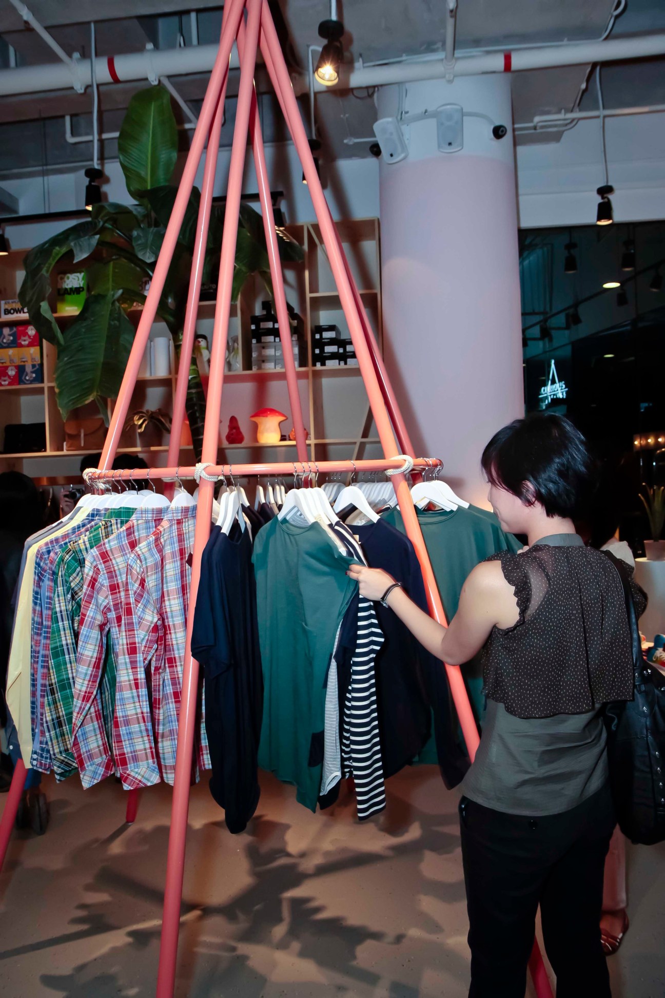 A woman browses clothing hung on a pink triangular display structure in A Curious Teepee shop.