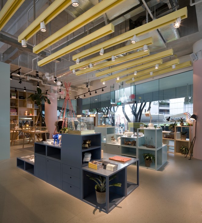 Modern retail interior with yellow ceiling beams, display shelving, and large windows overlooking a tree-lined street.