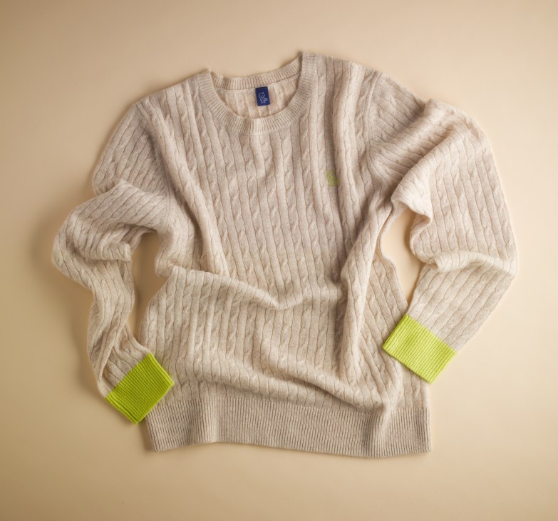 Cream cable-knit sweater with neon yellow-green cuff details on a beige background.