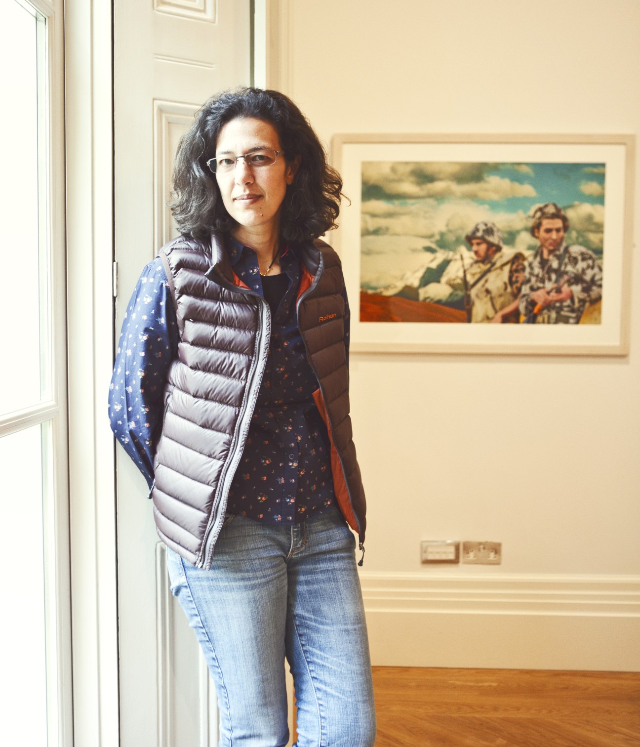Nermine Hammam stands in a gallery with a framed military artwork visible on the wall behind her.